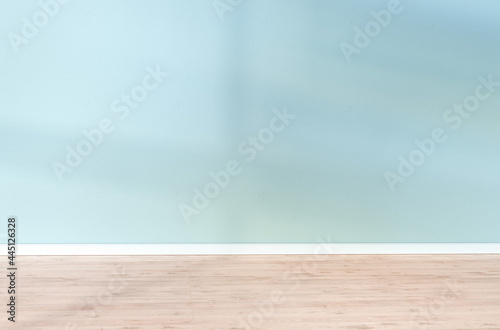 Light blue textured wall and wooden floor in empty room for displaying your product, light coming through window.