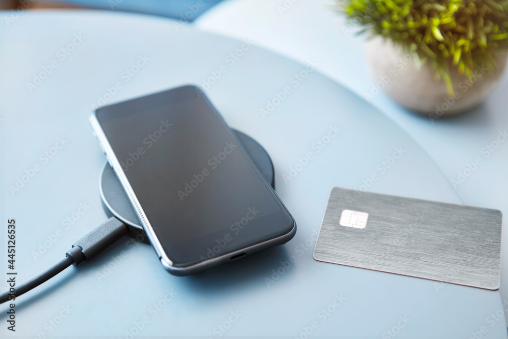 Wireless charging of modern black smartphone on table next to electronic chip access card. Wireless charging of modern black smartphone on table next to electronic chip access card.