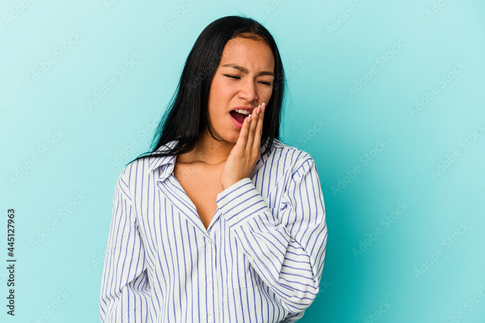 Young Venezuelan woman isolated on blue background yawning showing a tired gesture covering mouth with hand. Young Venezuelan woman isolated on blue background yawning showing a tired gesture covering mouth with hand.
