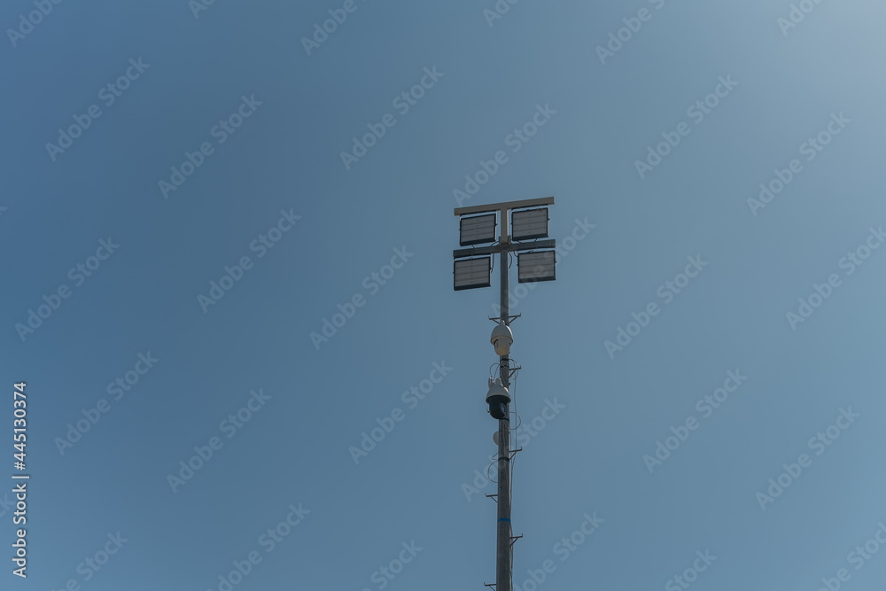 A street pole with surveillance cameras, in a criminal zone, and night lighting lamps. Against the blue sky. A street pole with surveillance cameras, in a criminal zone, and night lighting lamps. Against the blue sky.