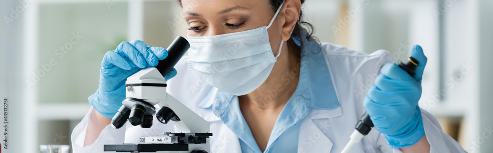 African american scientist in medical mask holding electronic pipette near microscope, banner African american scientist in medical mask holding electronic pipette near microscope, banner