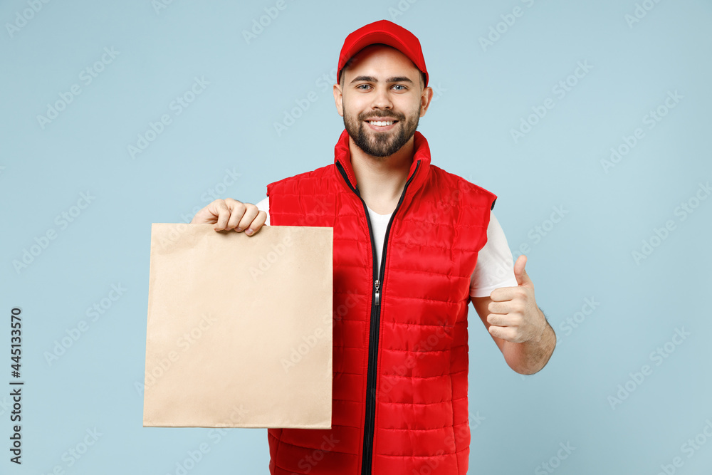 Delivery guy employee man in red cap white T-shirt vest uniform work as dealer courier service hold brown clear blank craft paper takeaway bag mock up isolated on pastel blue color background studio. Delivery guy employee man in red cap white T-shirt vest uniform work as dealer courier service hold brown clear blank craft paper takeaway bag mock up isolated on pastel blue color background studio.