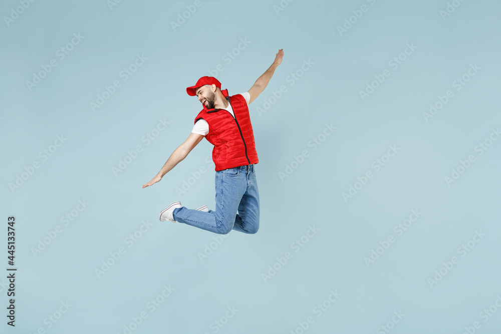 Full size body length side view delivery guy employee man in red cap white T-shirt vest uniform work dealer courier jump run go walk isolated on pastel blue color background studio. Service concept Full size body length side view delivery guy employee man in red cap white T-shirt vest uniform work dealer courier jump run go walk isolated on pastel blue color background studio. Service concept