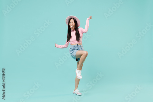 Full size body length fun laughing happy jubilant young brunette asian woman 20s wears pink clothes standing on one leg wink spreading hands isolated on pastel blue color background studio portrait © ViDi Studio