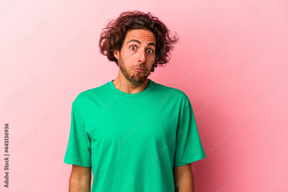 Young caucasian man isolated on pink bakcground shrugs shoulders and open eyes confused. Young caucasian man isolated on pink bakcground shrugs shoulders and open eyes confused.