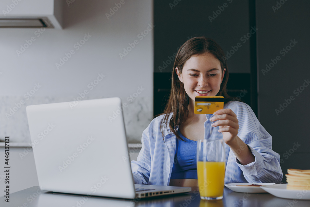 Young housewife woman in casual clothes blue shirt use laptop pc computer credit bank card shopping online order delivery book tour cook food in light kitchen at home. Healthy diet lifestyle concept. Young housewife woman in casual clothes blue shirt use laptop pc computer credit bank card shopping online order delivery book tour cook food in light kitchen at home. Healthy diet lifestyle concept.