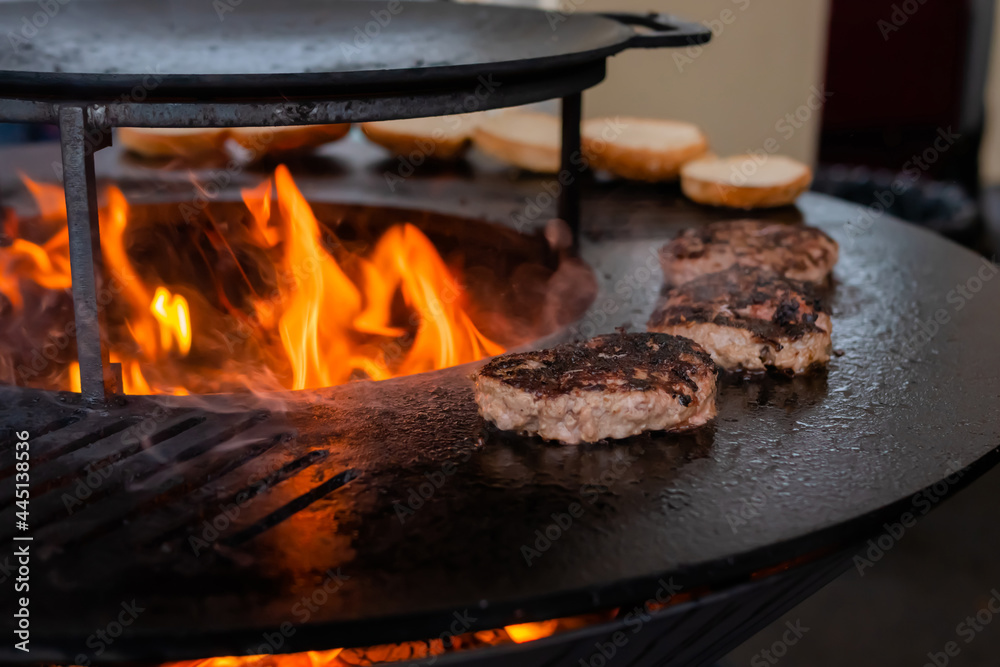 Process of grilling fresh meat cutlets for burgers on brazier with hot flame at summer local food market - close up view. Outdoor cooking, gastronomy, cookery, street food concept Process of grilling fresh meat cutlets for burgers on brazier with hot flame at summer local food market - close up view. Outdoor cooking, gastronomy, cookery, street food concept