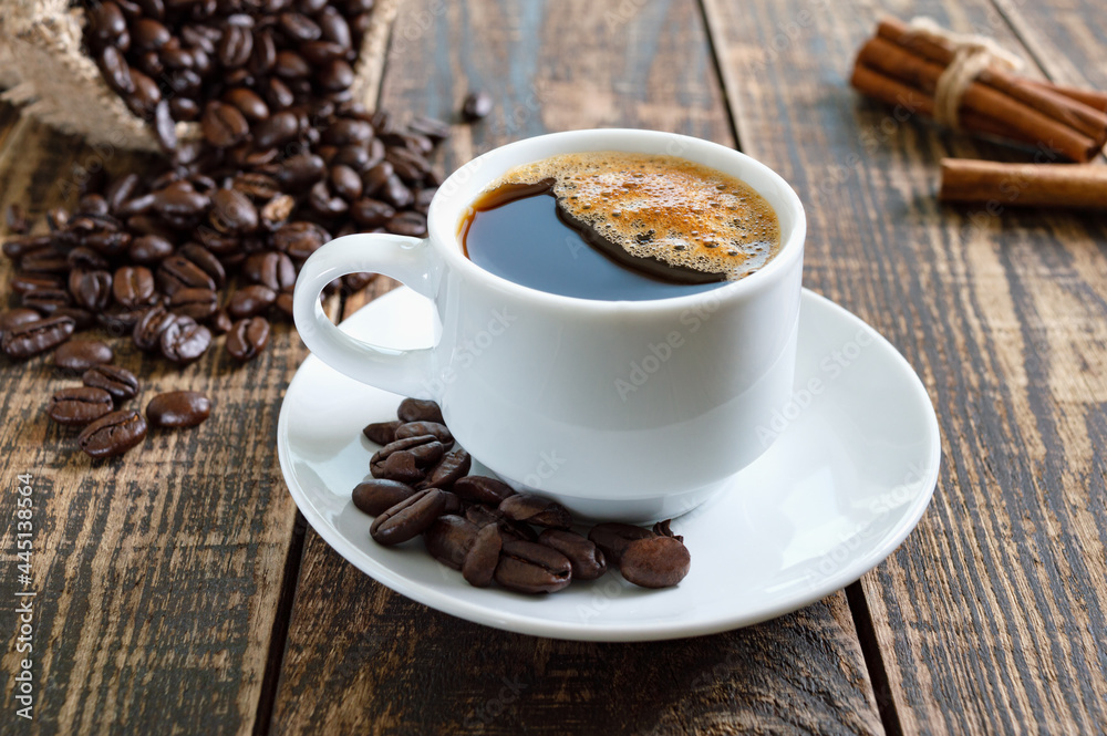 Fototapeta premium A cup of coffee, a bag with roasted coffee beans, cinnamon on a rustic background.