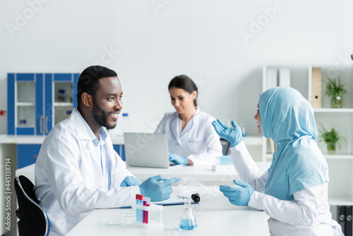 Smiling multiethnic scientists talking near medical equipment in laboratory