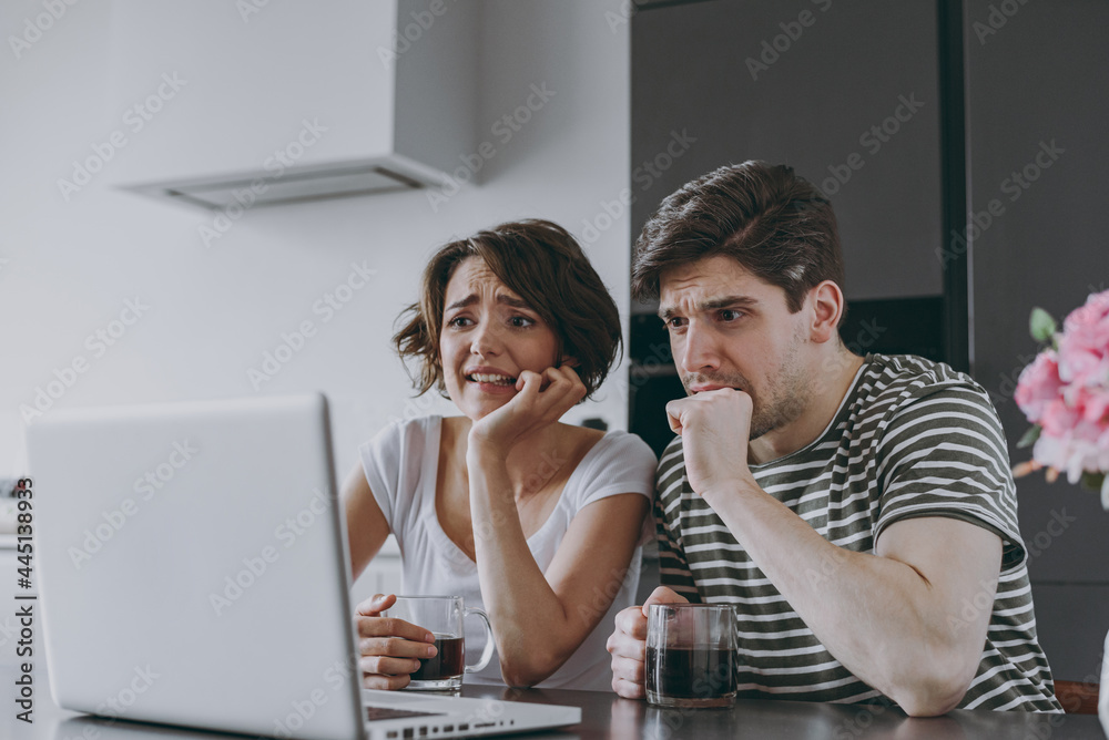 Young sad confused couple two woman man in casual t-shirt clothes sit table drink coffee using laptop pc computer ith virus do oops gesture in light kitchen at home together People lifestyle concept. Young sad confused couple two woman man in casual t-shirt clothes sit table drink coffee using laptop pc computer ith virus do oops gesture in light kitchen at home together People lifestyle concept.