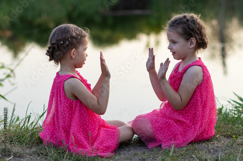 Little girls in pink dresses playing on the shore of the pond in summer