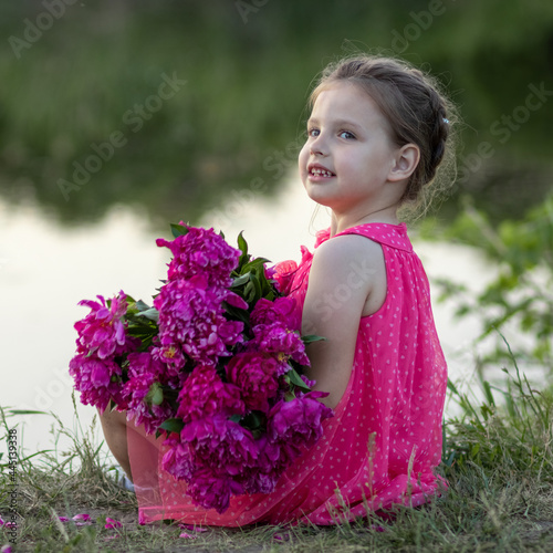 Little girl sitting with a bouquet of flowers on the shore of the pond
