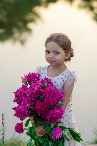 Little girl standing with a bouquet of peonies near the pond