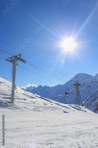 The supports of the cable car at the ski resort. There is a blue sky and a bright sun on the background