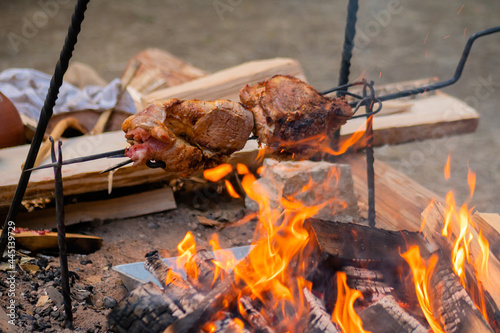 Process of cooking large meat peaces on spit over open fire at historical festival - close up view. Outdoor cooking, travelling, camping, reenactment concept