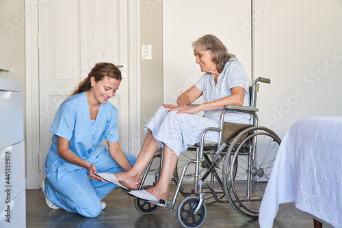 Altenpflegerin hilft Seniorin im Rollstuhl beim Schuhe anziehen