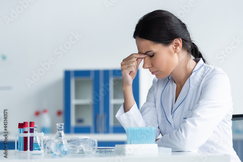 Side view of tired scientist sitting near flasks and test tubes