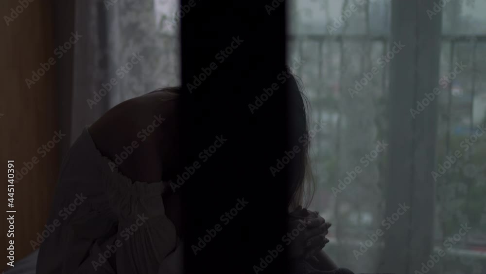 Depressed Asian woman sitting alone on the bed in the dark with cuddle herself and crying. Loneliness sad female think grief trouble life problem in bedroom. Negative emotion and mental health concept