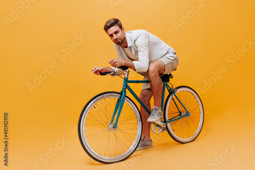 Handsome bearded man with brown hair in cool t-shirt and beige modern shorts posing with bicycle and looking into camera.. photo