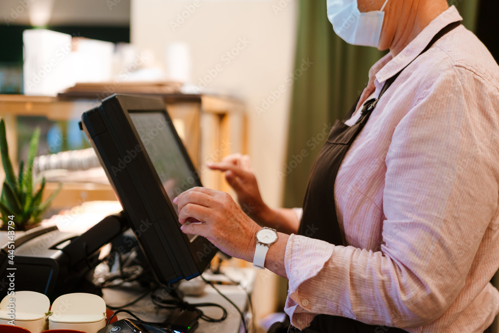 Mature woman wearing face mask working at cash register in cafe