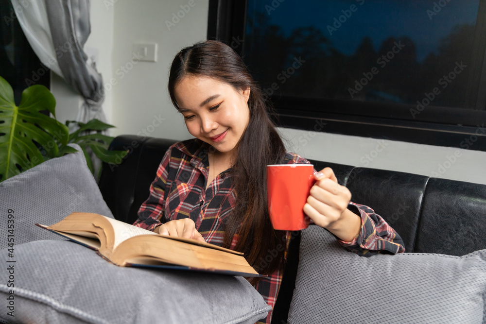 Young asian woman with coffee cup and read book on bed in bedroom interior Young asian woman with coffee cup and read book on bed in bedroom interior