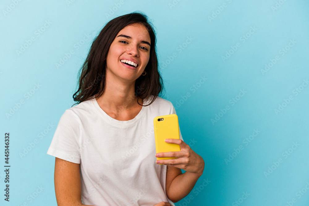 Young caucasian woman holding a mobile phone isolated on blue background laughing and having fun. Young caucasian woman holding a mobile phone isolated on blue background laughing and having fun.