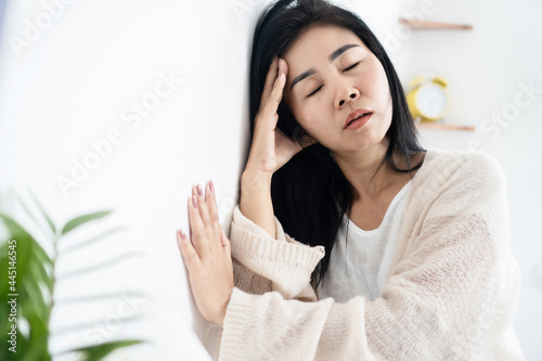 Asian woman having problem with Meniere's disease, fainting or dizziness hand holding her head leaning against the wall photo