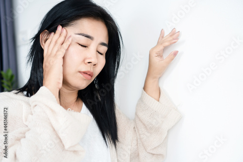 Asian woman having problem with Meniere's disease, fainting or dizziness hand holding her head leaning against the wall photo