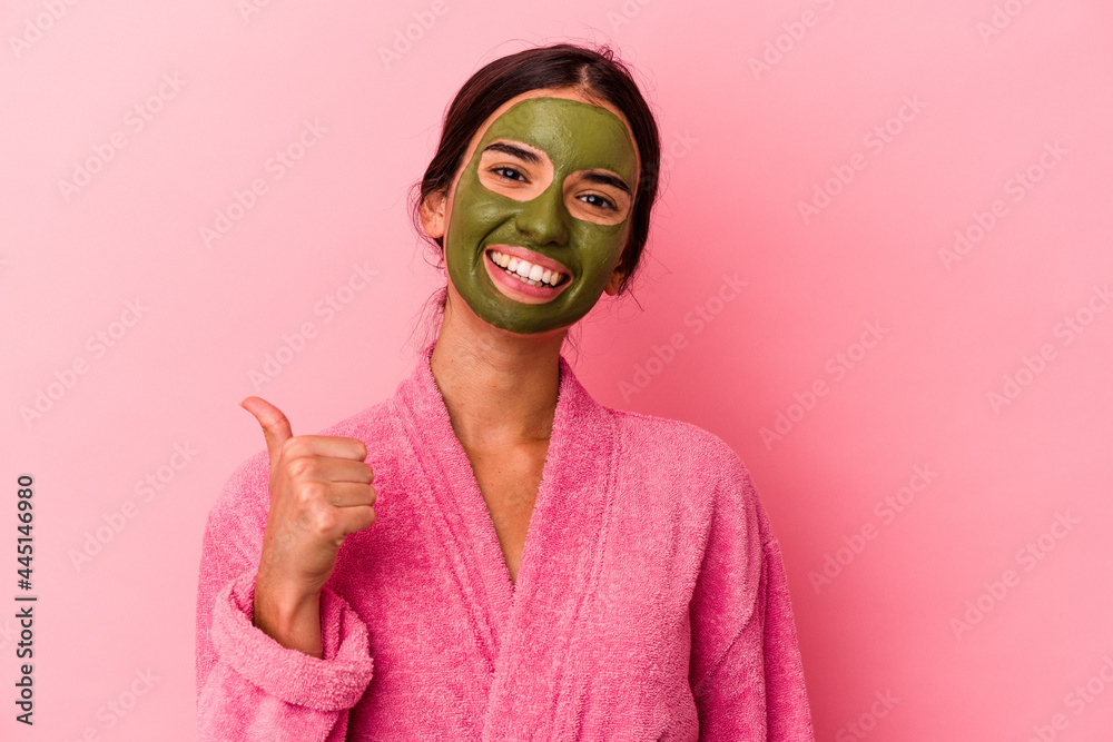 Young caucasian woman wearing a bathrobe and facial mask isolated on pink background smiling and raising thumb up Young caucasian woman wearing a bathrobe and facial mask isolated on pink background smiling and raising thumb up