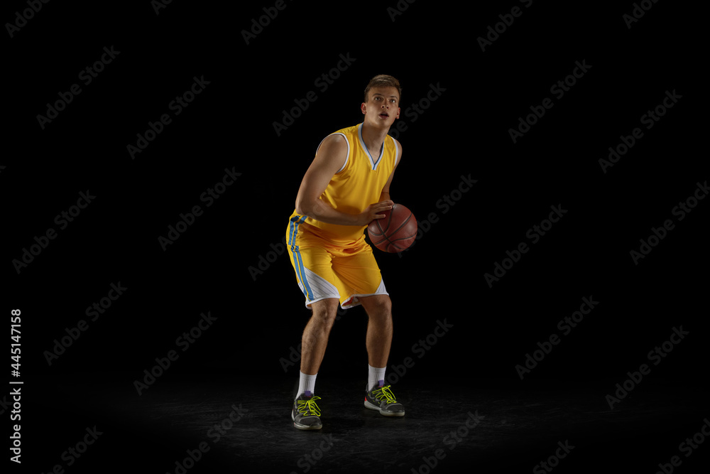One young man, basketball player with a ball training isolated on dark black studio background. Advertising concept. Fit Caucasian athlete practicing with ball. One young man, basketball player with a ball training isolated on dark black studio background. Advertising concept. Fit Caucasian athlete practicing with ball.