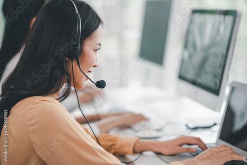 Team of call center staff in Asia wears headphones with a microphone. Smile while serving customers at desks and computers. Service concept and consulting. Communication concept.