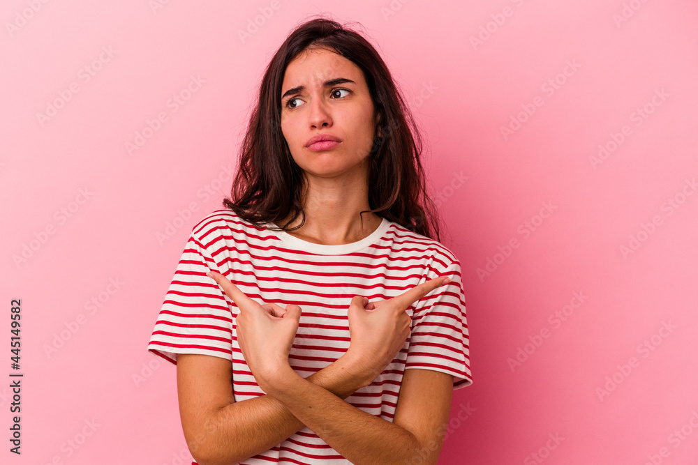 Young caucasian woman isolated on pink background points sideways, is trying to choose between two options. Young caucasian woman isolated on pink background points sideways, is trying to choose between two options.