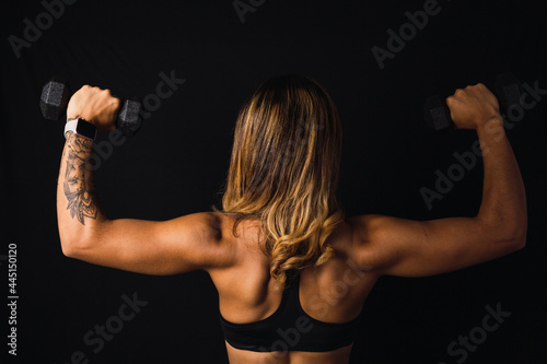 Image of a Latina woman's back in shape with weights on a dark background.