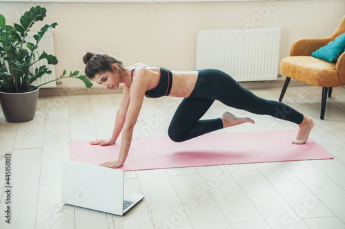 brunette woman is wearing sport clothes during a fitness session at home using a laptop