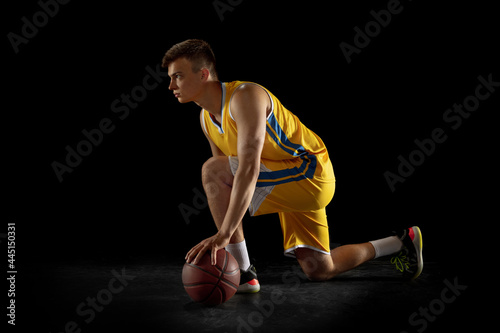 Portrait of young man, basketball player with a ball posing isolated on dark black studio background. Advertising concept. Before game, match