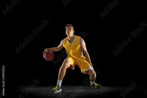 Basketball player with a ball in action and motion isolated on dark black studio background. Advertising concept. Strong Caucasian athlete practicing with basketball ball. © master1305