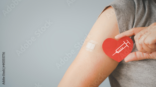 Leinwand Poster senior woman holding red heart shape with  syringe and showing her arm with band