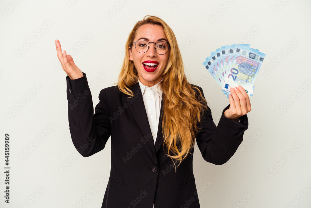 Obraz premium Caucasian business woman holding bills isolated on white background receiving a pleasant surprise, excited and raising hands.