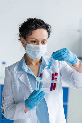 African american scientist in latex gloves and medical mask holding test tubes with samples