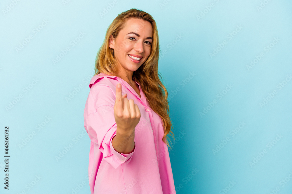Caucasian woman isolated on blue background pointing with finger at you as if inviting come closer. Caucasian woman isolated on blue background pointing with finger at you as if inviting come closer.
