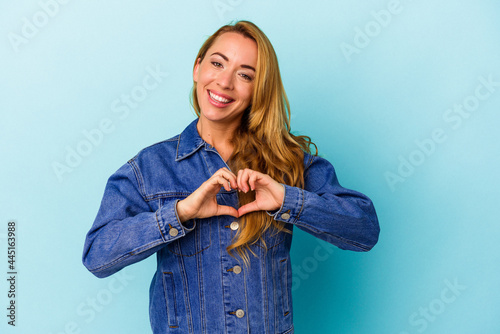 Caucasian woman isolated on blue background smiling and showing a heart shape with hands. photo