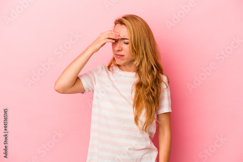Caucasian blonde woman isolated on pink background having a head ache, touching front of the face.