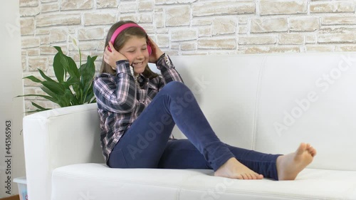 Pretty young girl dancing and listening music with headphones on white sofa at home