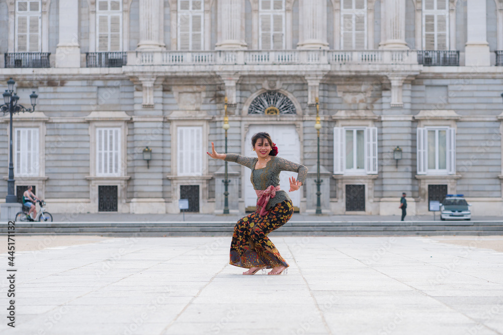 young happy Indonesian woman from Bali having vacation in Europe - beautiful and exotic Balinese tourist girl dancing in traditional outfit touring in the city enjoying holidays