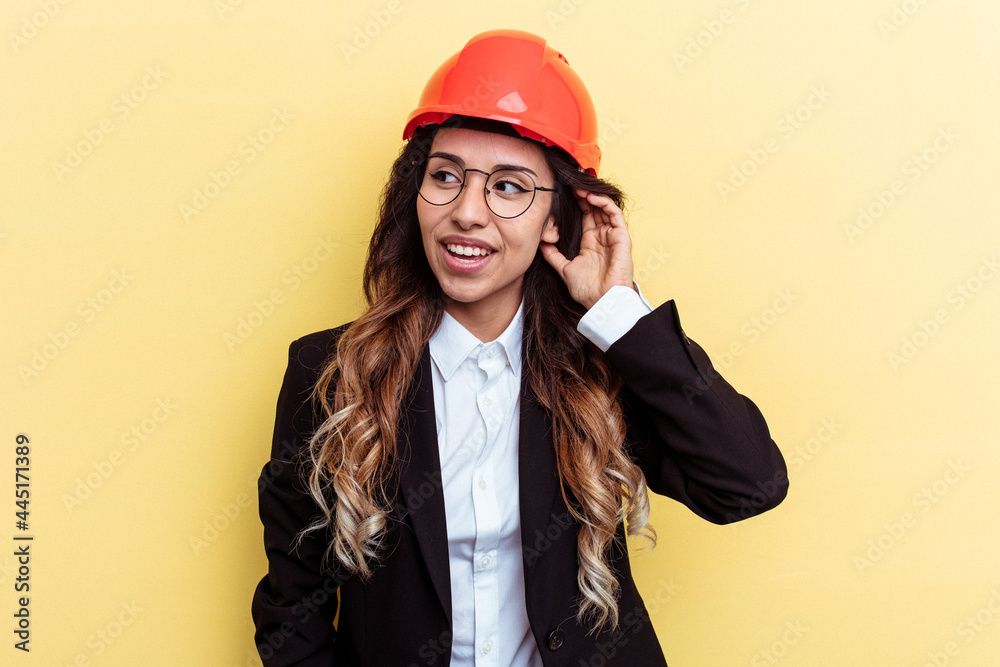 Young architect mixed race woman isolated on yellow background trying to listening a gossip.