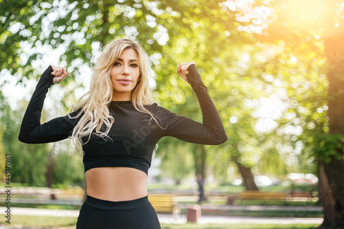 Woman standing posing showing body biceps abdominal muscles outside green park morning looking away. Athletic lady dressed fitness sportwear clothes. Healthy lifestyle, sport recreation. Copy space  © Volodymyr