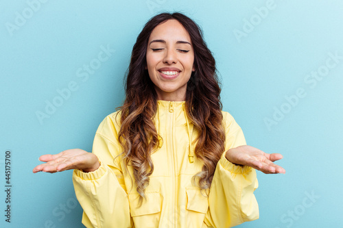 Young mexican woman isolated on blue background holding something with palms, offering to camera.