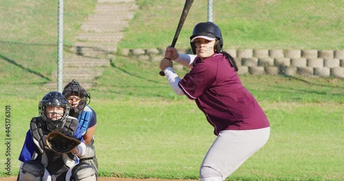 Diverse group of female baseball players playing on the field, hitter swinging for pitched ball