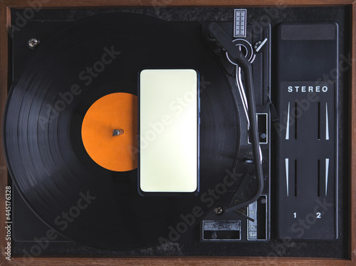 The top view of the new modern smartphone is on the music record on the turntable. The phone has a white screen. Music. Application. Copy space.