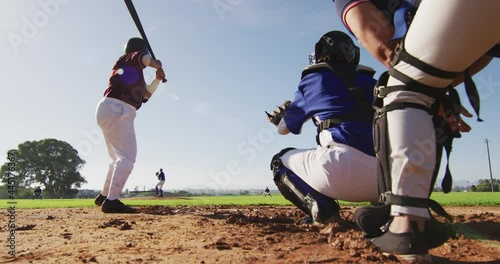 Diverse group of female baseball players playing on the field, hitter hitting pitched ball